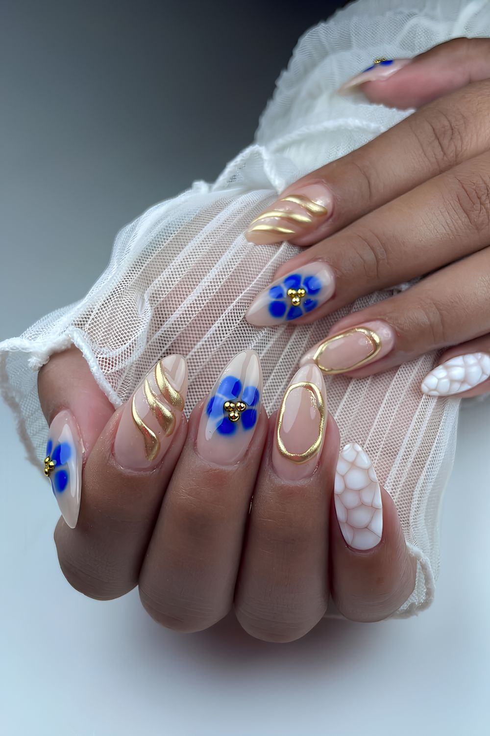 Neutral nails with white animal print, blue blooming gel florals and gold chrome accents