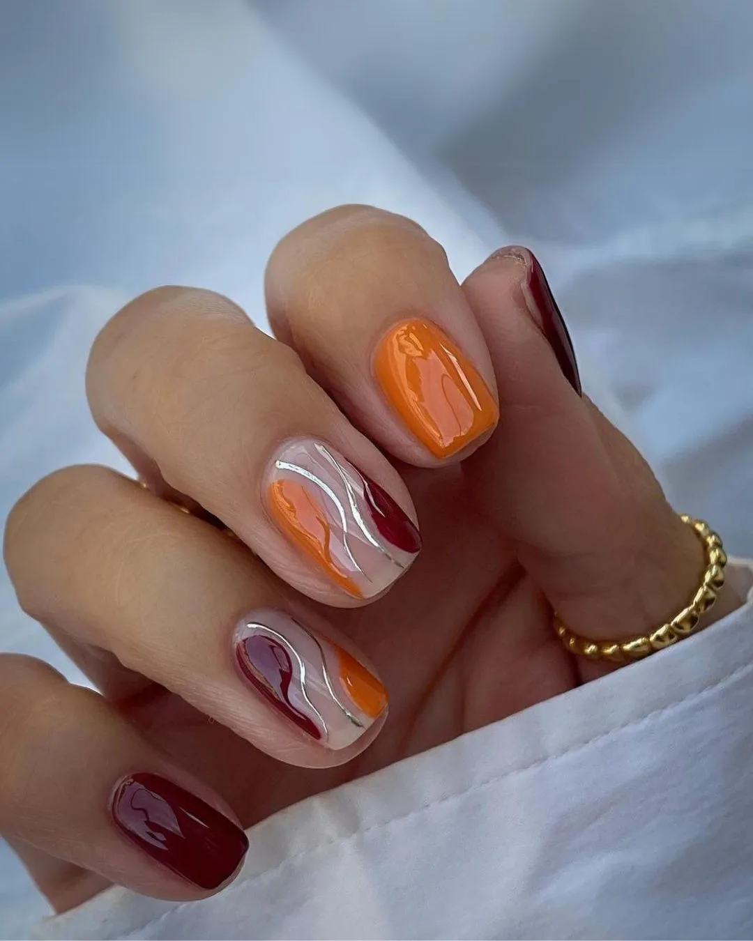 Burgundy and orange nails with silver accent lines