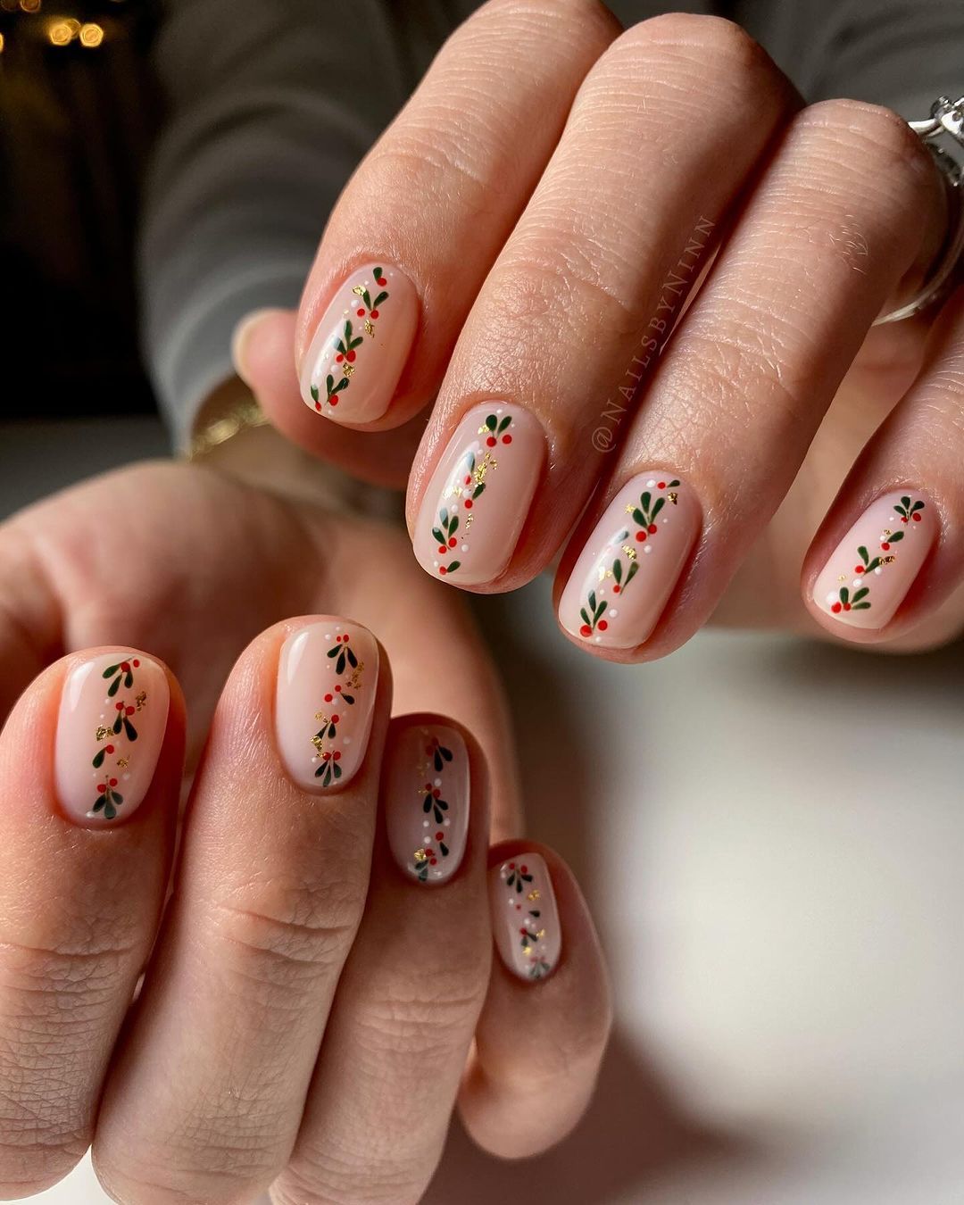 Nude nails with a row of tiney holly designs and subtle gold accents