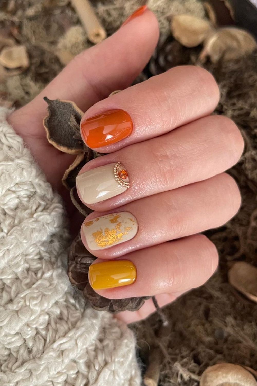 Orange and mustard yellow nails with gold and gem accents