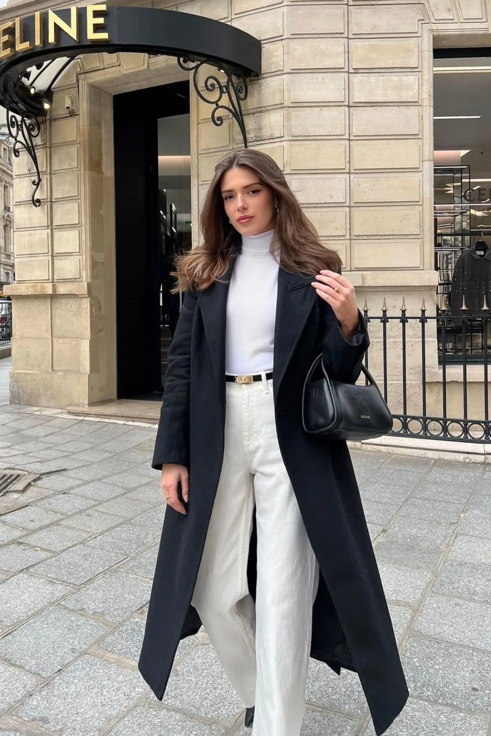 long black coat over white trousers and turtleneck