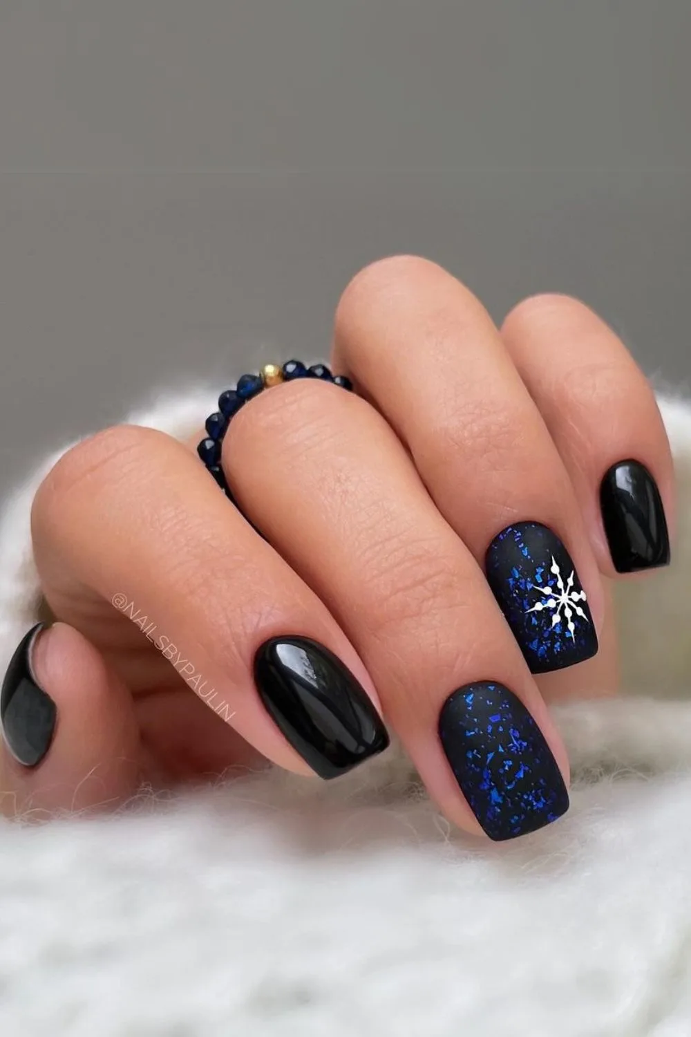 Black nails with midnight blue accent nails and white snowflake detail