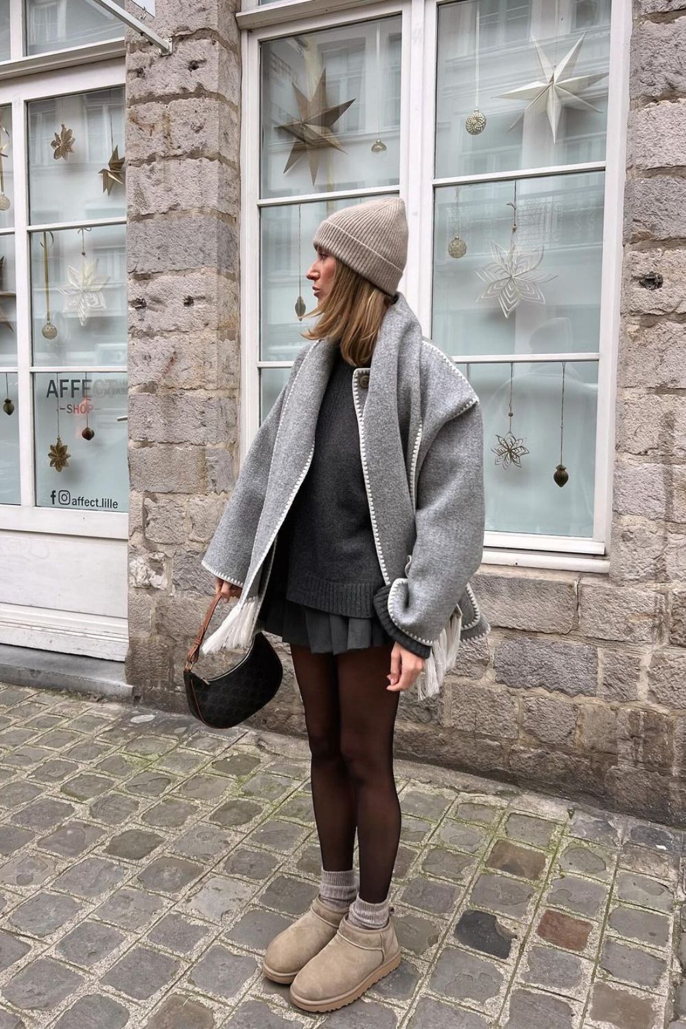 Light gray jacket over dark grasy skirt and sweater paired with mini uggs