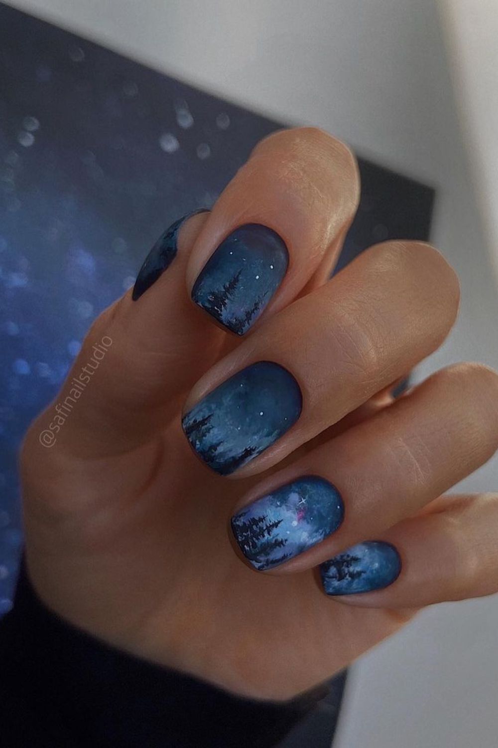 Matte midnight blue nails with intricate forest silhouettes and twinkling stars