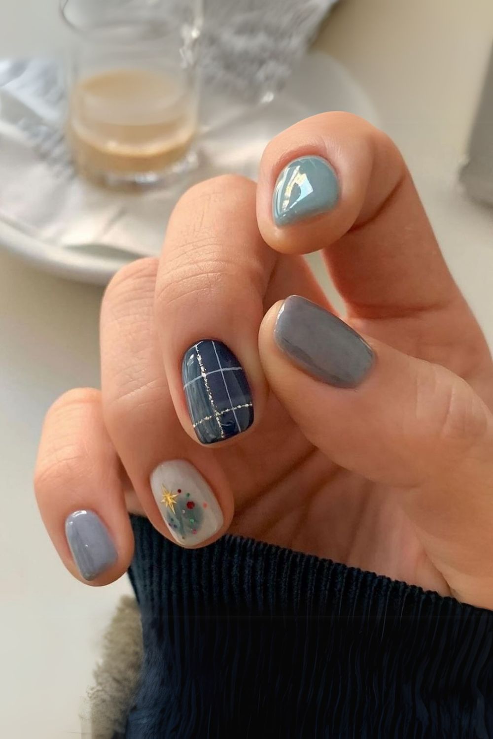 Mix of muted blue, navy plaid with silver lines, and a white accent nail decorated with a tiny Christmas tree motif