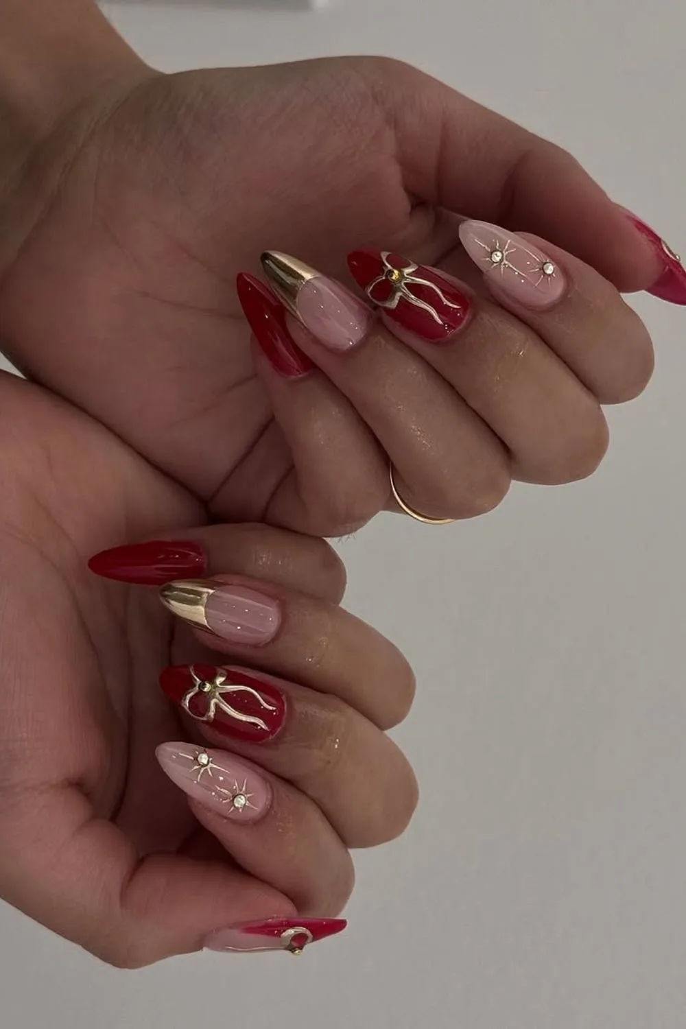 Solid red nails with chrome French tips and bow details and gold celestial rhinestone details on accent nails