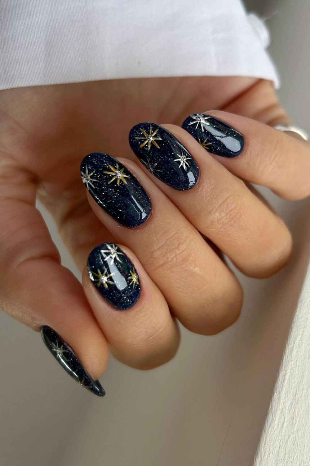 Starry night design featuring dark blue nails with subtle silver glitter and gold chrome stars