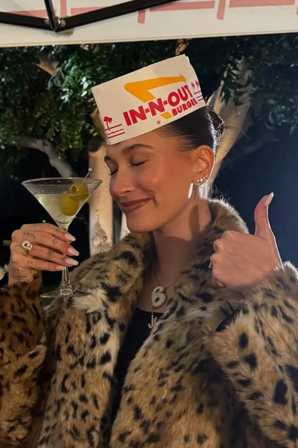 Hailey Bieber with milky nails holding martini and a paper hat