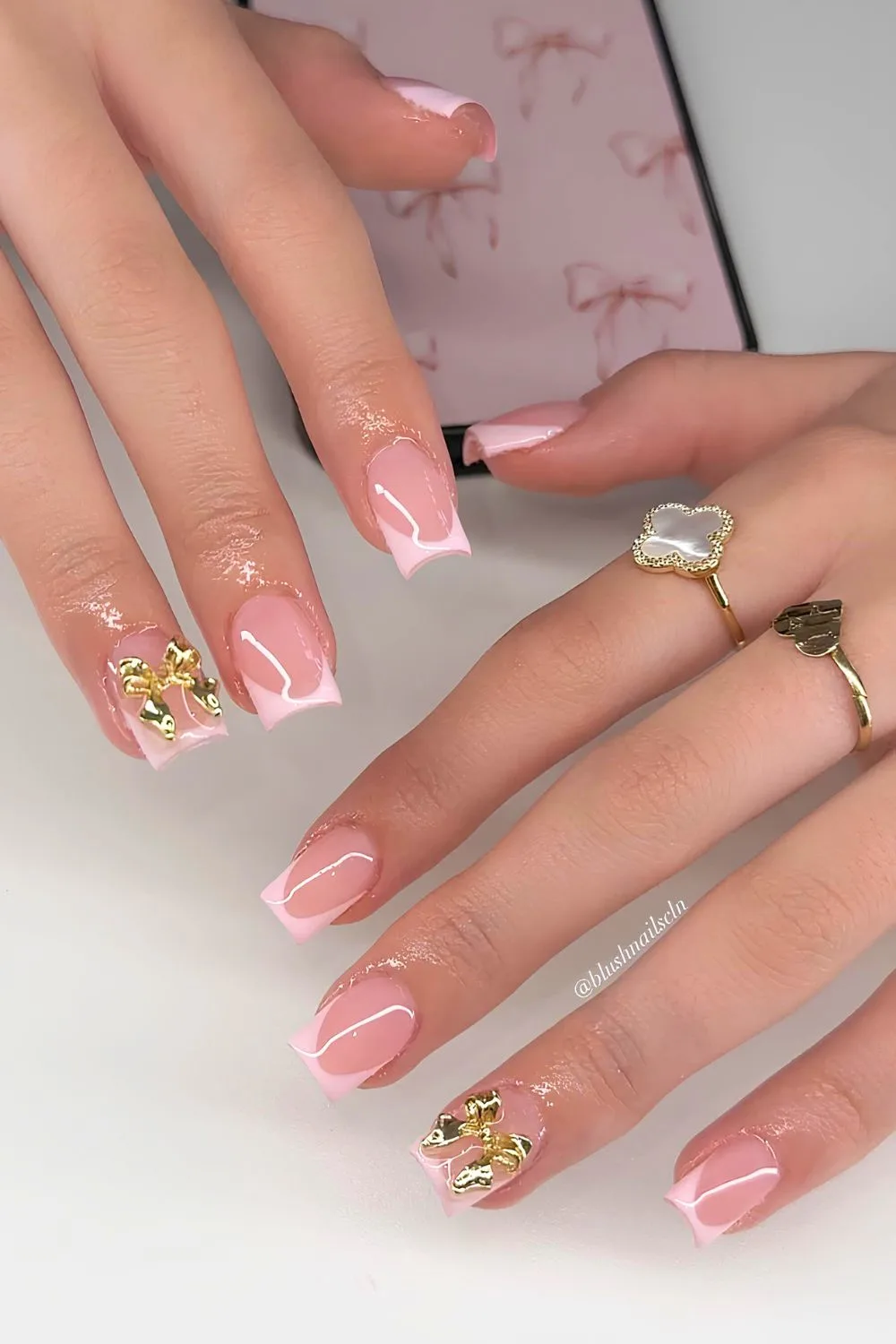 Pink French tip nails with gold 3D bow accent