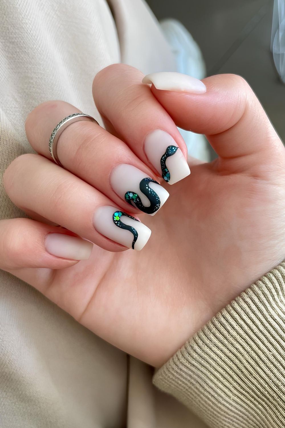 White matte nails with glittery green snake design spanning across three nails