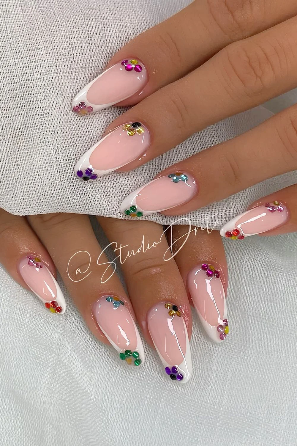 White French tip nails with colorful rhinestone flowers and glossy finish