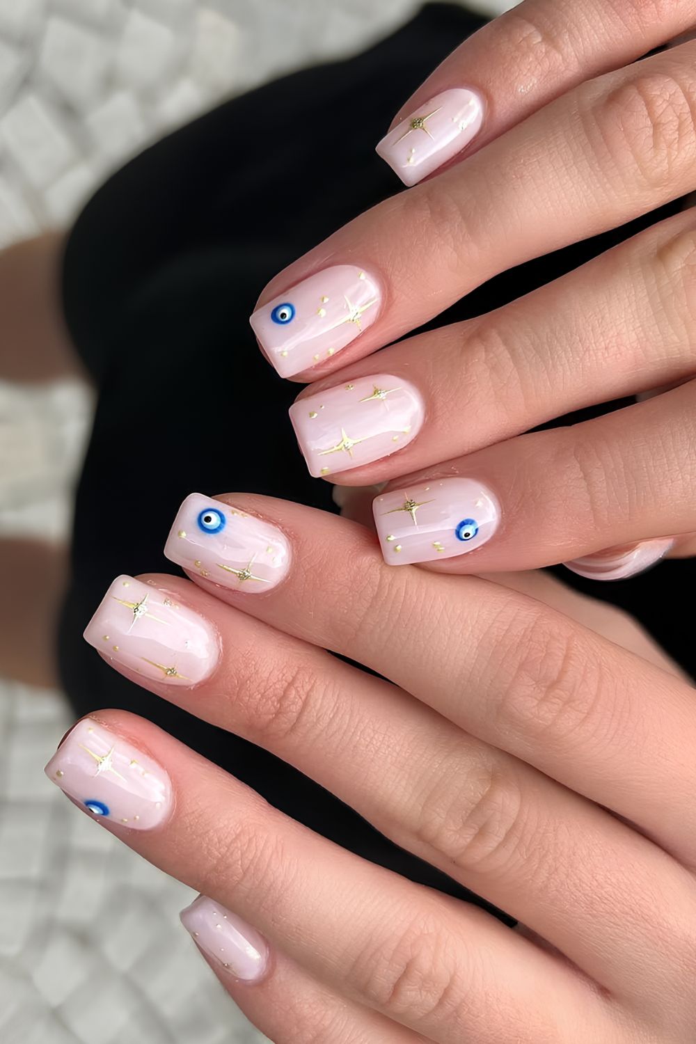 Milky pink BIAB nails with gold starburst and evil eye designs