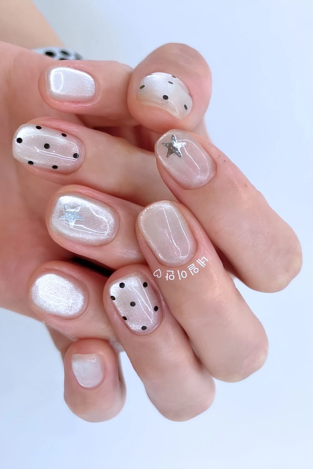 Light gray cat eye nails with black polka dots and silver stars