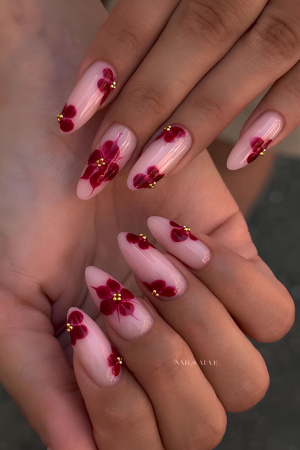 Sheer pink almond nails with cherry red florals and gold studs