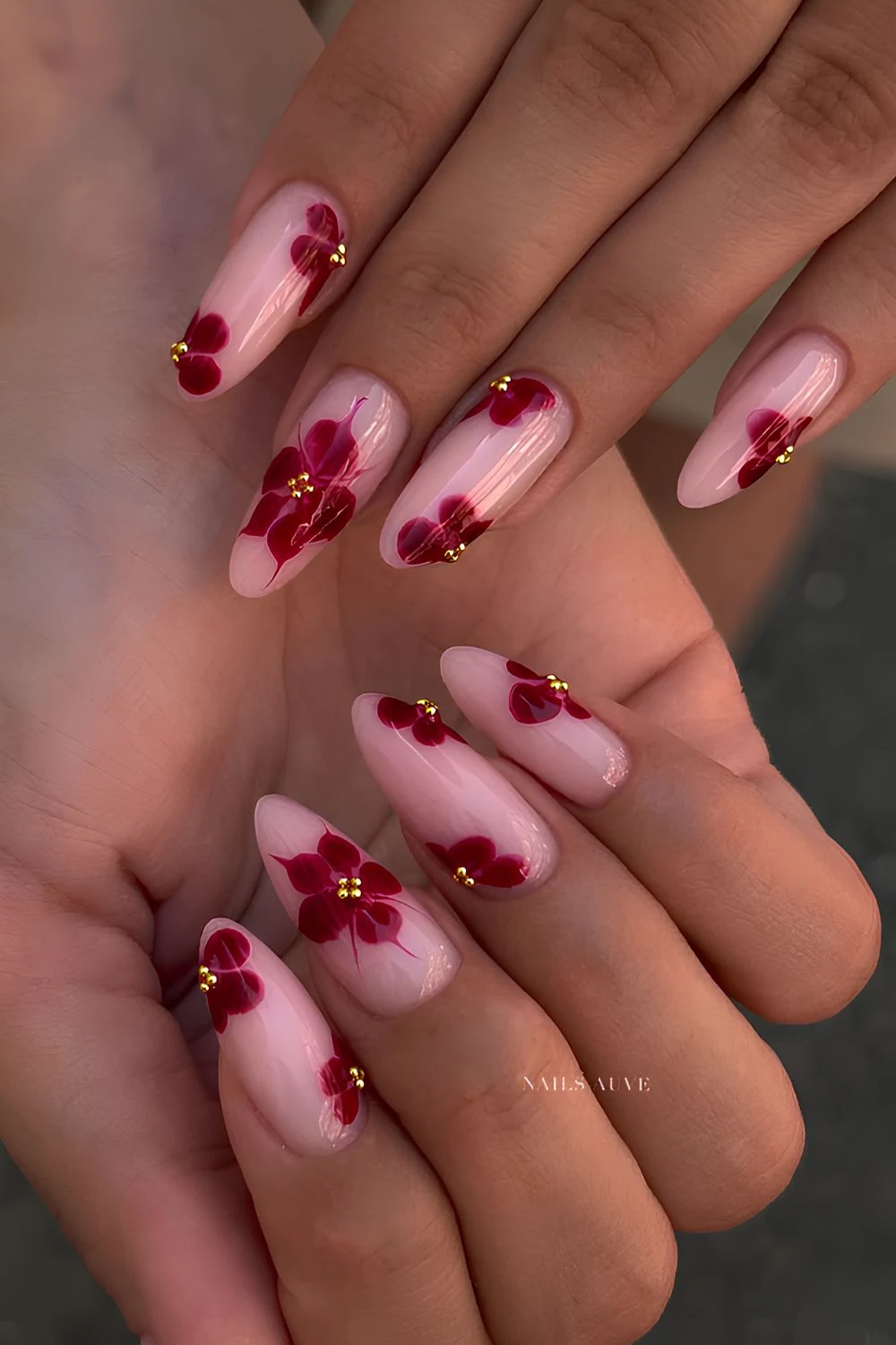 Sheer pink almond nails with cherry red florals and gold studs