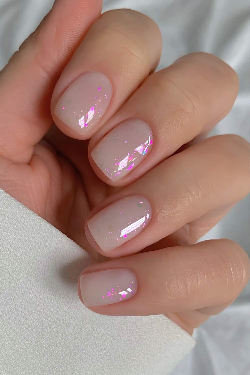 Opal-inspired milky white nails with pink glitter flakes