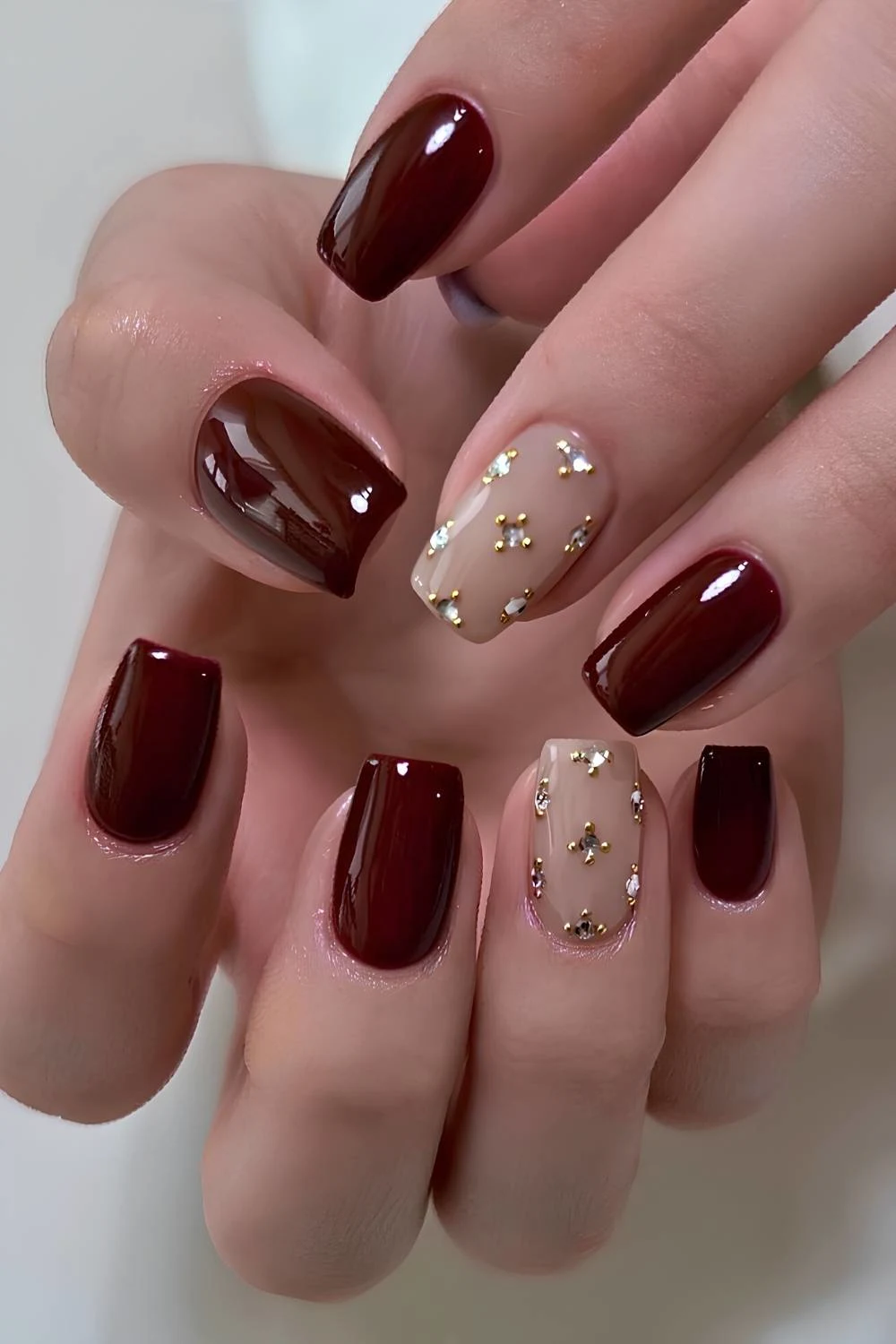 Dark red nails with rhinestones and gold beads